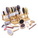 A set of pet grooming tools and brushes displayed on a white background, including wooden stands, brushes, combs, a nail grinder, and a lick mat.
