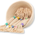Natural fiber toy with colorful tassels inside a woven basket on a white background